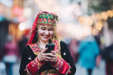 A cheerful woman in traditional clothing using her smartphone during a festive moment, showing how easily the BDJL app fits into everyday life.